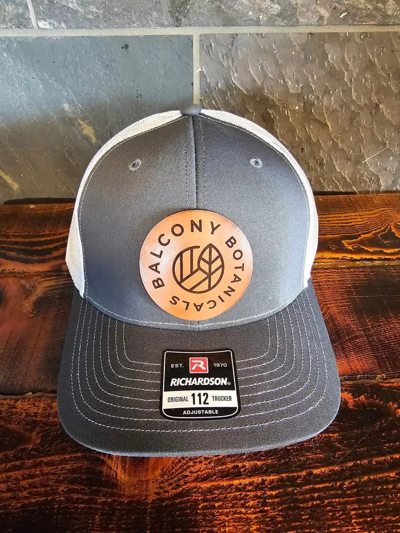 Charcoal and white trucker hat with a round natural leather Balcony Botanicals patch