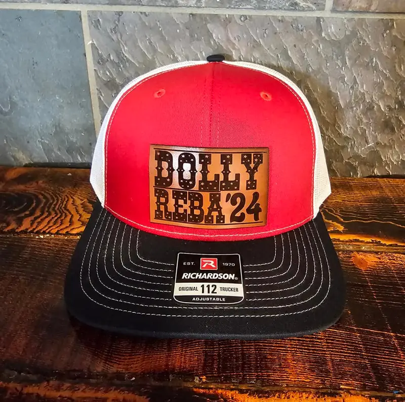 Red and white trucker hat with a rust leather Dolly Reba '24 patch