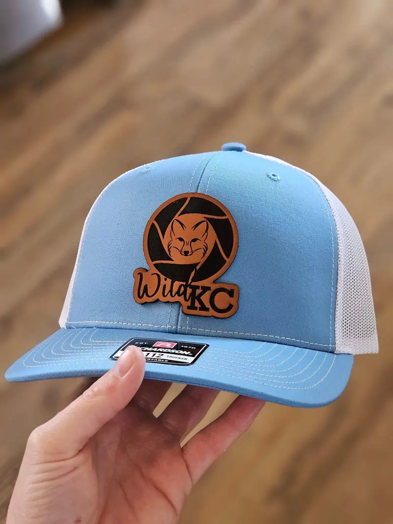 Light blue and white trucker hat with a round rust leather Wild KC patch