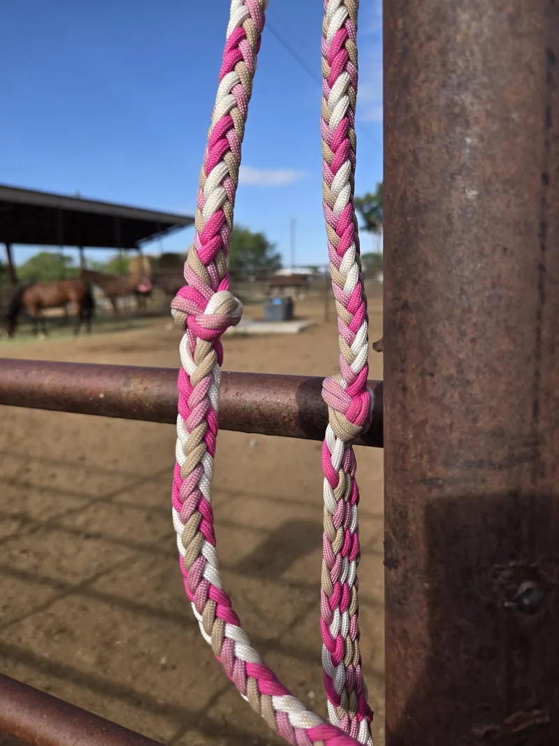 Close-up of Pink Pony Club braided reins with grip knots, hanging on a fence post